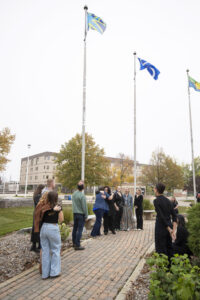 People looking upwards at the newly raised Deaf Flag outside RRC Polytech's Notre Dame Campus.