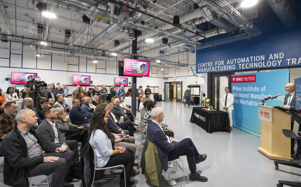 Guests seated in rows listen to podium presentations at RRC Polytech's new Centre for Automation and Manufacturing Technology Transfer.