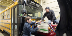 Two men working on the engine of a converted school bus in the climatic chamber of ... RRC Polytech's Vehicle Technology & Energy Centre.