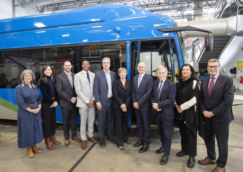 Group of men and women standing in front of a blue electric transit bus.