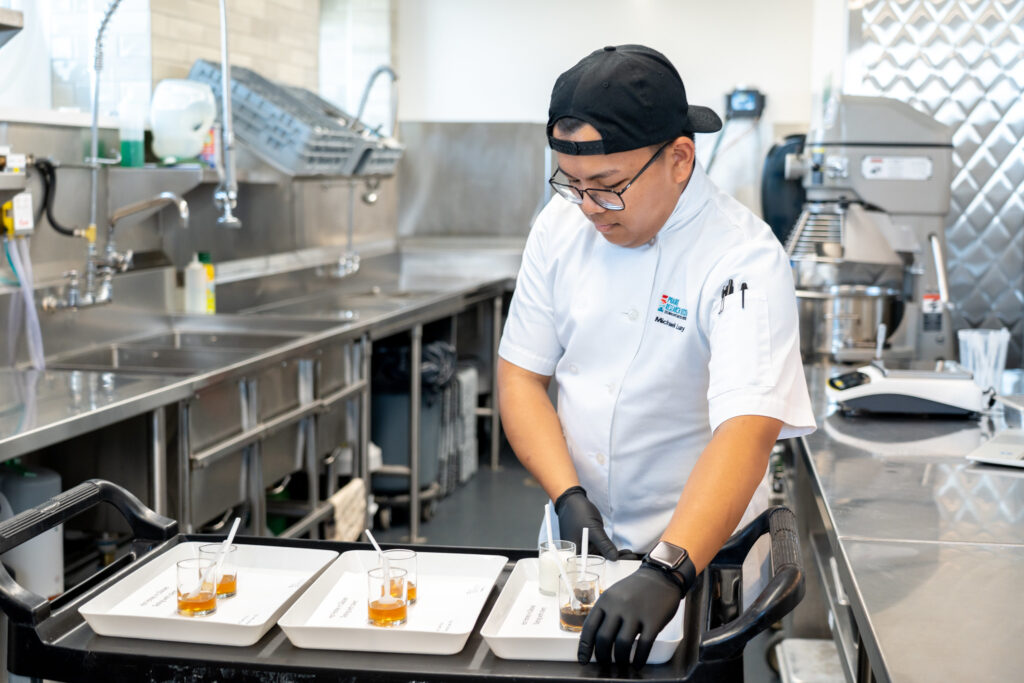 Culinary researcher in white smock staging trays of honey in small jars.