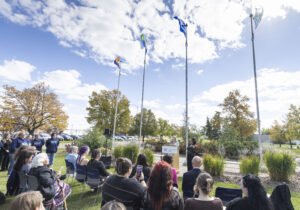 Families Minister Nahanni Fontaine speaks at an outdoor podium flanked by flagpoles.