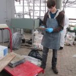 Making notes on a clipboard, a student performs a waste audit in a warehouse.