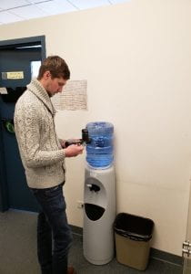 A man reads a meter in front of a water cooler.