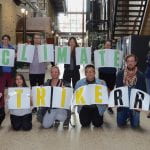 18 RRC Polytech Students and staff standing in the Roblin Atrium holding a sign that says #ClimateStrikeRRC