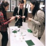 Three students cutting green circles out of felt to make pins, talking and laughing.