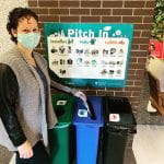 A woman with a mask putting an item into one of three bins with a sign above showing what waste goes in each bin.
