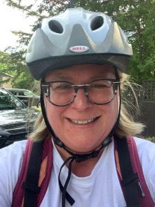 Woman with glasses smiling and wearing a bike helmet.