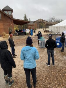 Several students standing around a waste and recycling bin while Renata explains the program.