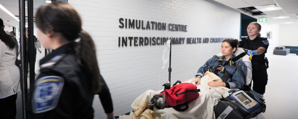Paramedicine students wheel a patient into a Simulation Centre on a stretcher.