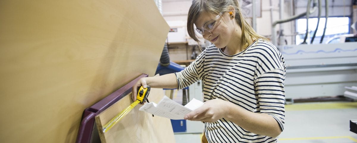 A woman is pictured taking measurements in the carpentry lab