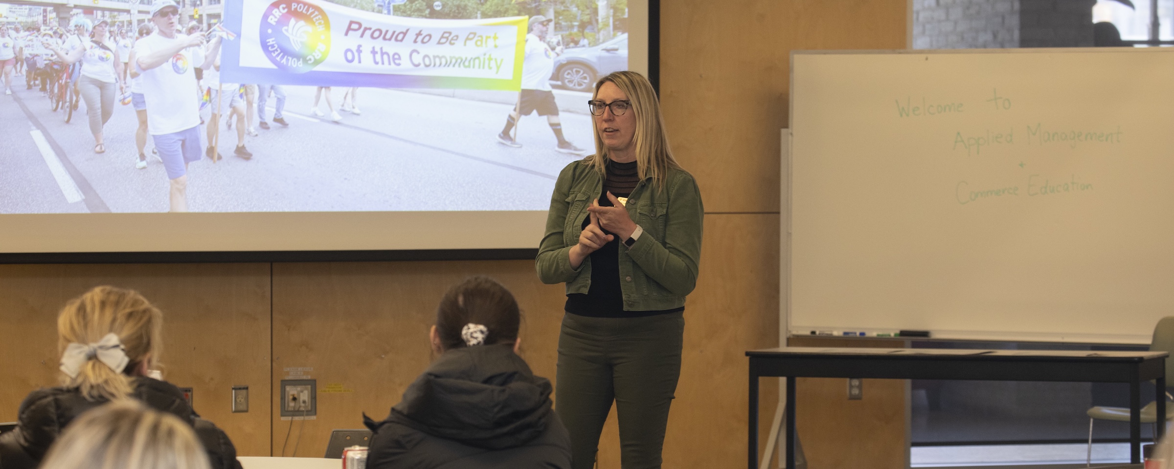 Instructor standing at the front of a classroom and talking to students who are sitting down