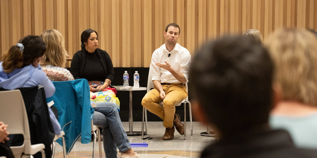 Group of people in a seminar with a man sitting down and speaking 