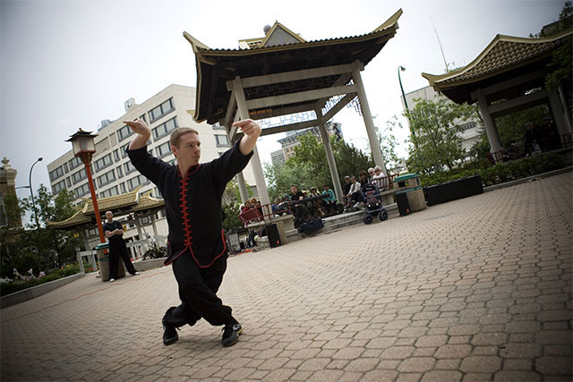 Instructor Sifu Josh Schafer strikes a tai chi pose in a courtyard with a pagoda in the background.