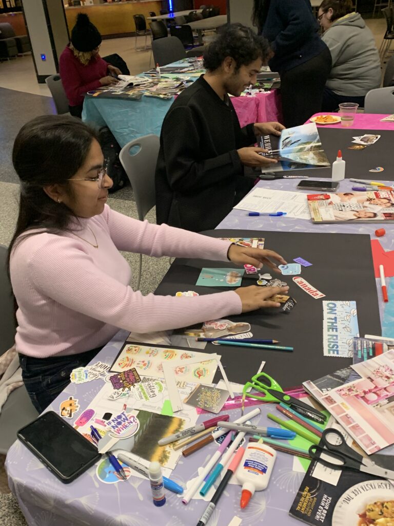 Students sitting at a table each with a piece of poster paper, and crafting materials scattered around including stickers, scissors, glue, magazines and markers.