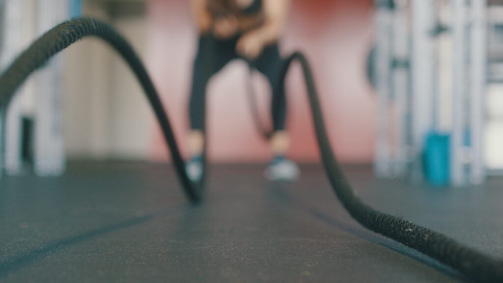 Photo of a female athlete using battle rope on fitness turf.