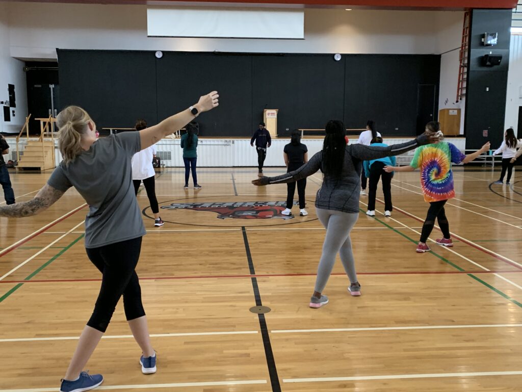 Group of students and staff learning how to breakdance in a gym