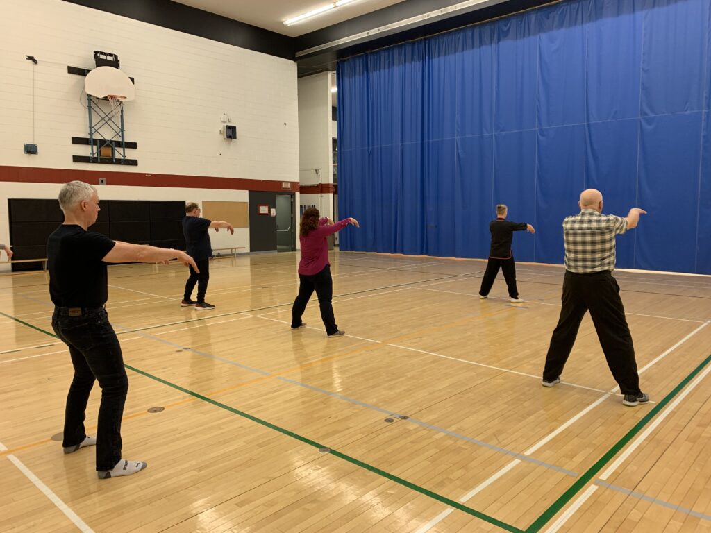 Group of college staff learning tai chi movements in a gym