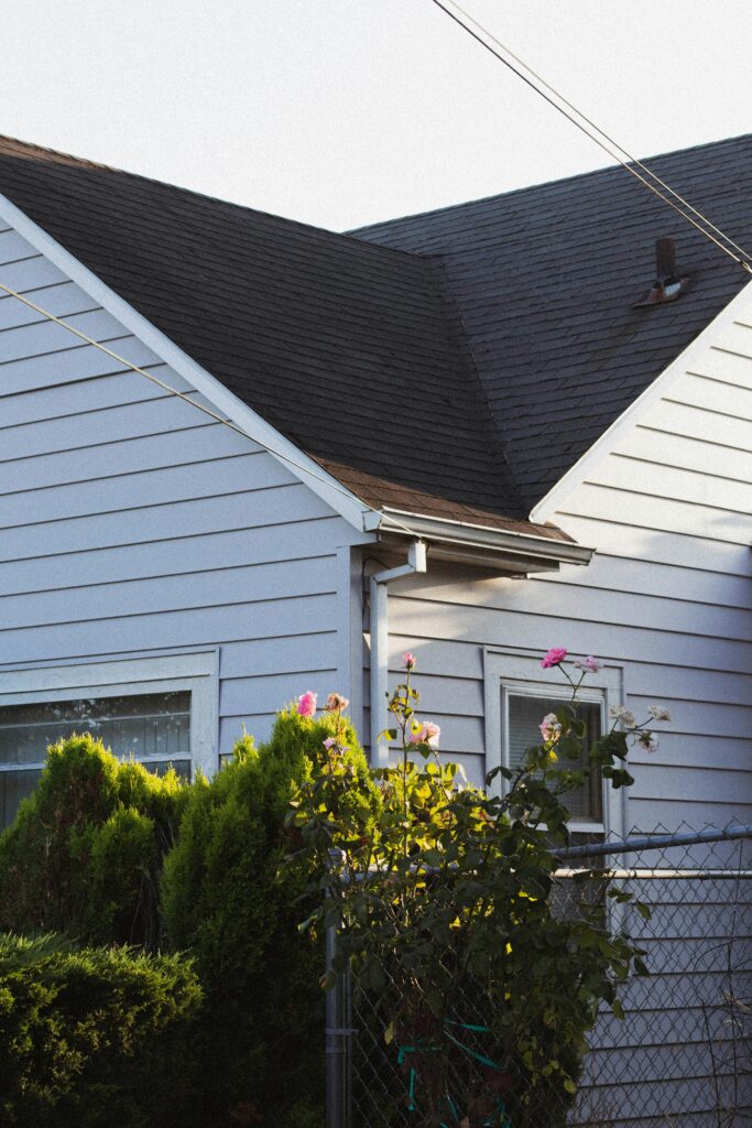 Side of house and roof with bushes in front.