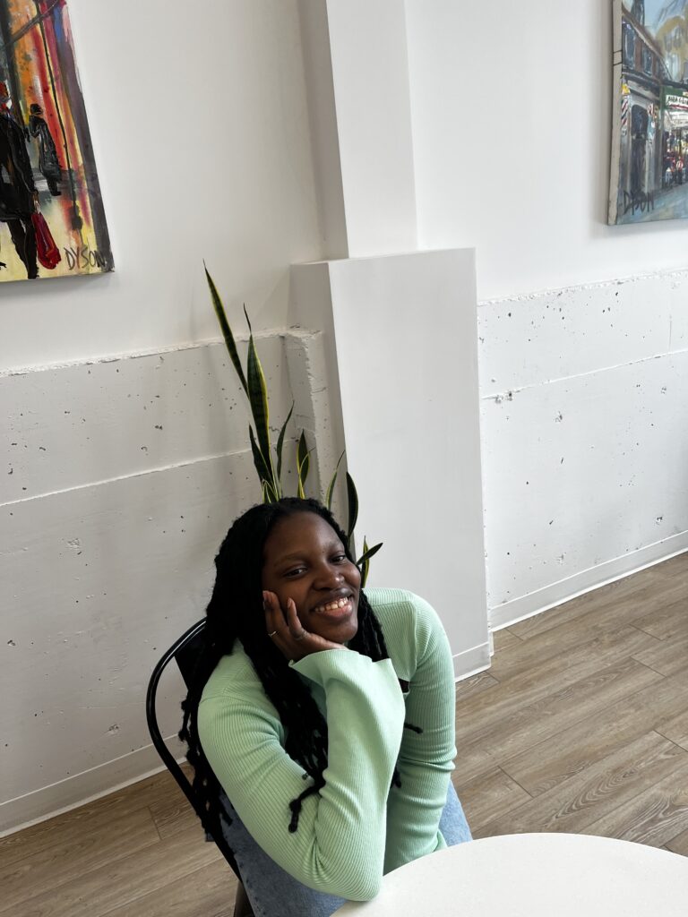 Woman sitting on a chair with her hand on her cheek, smiling.