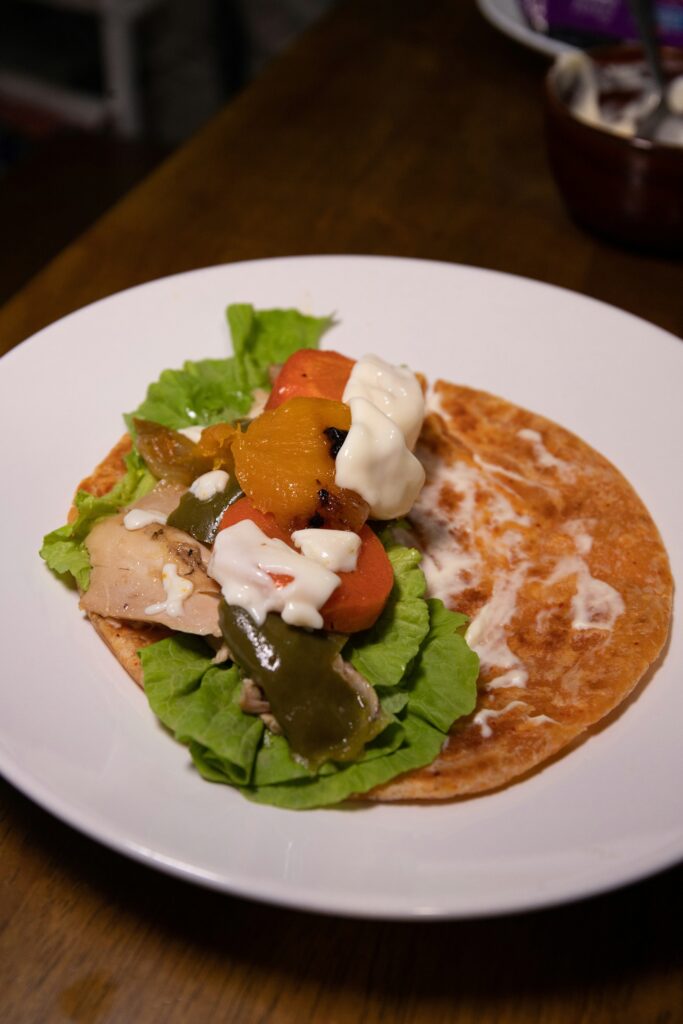 Open tortilla with chicken, sauce and vegetables on half of it, ready to roll up.