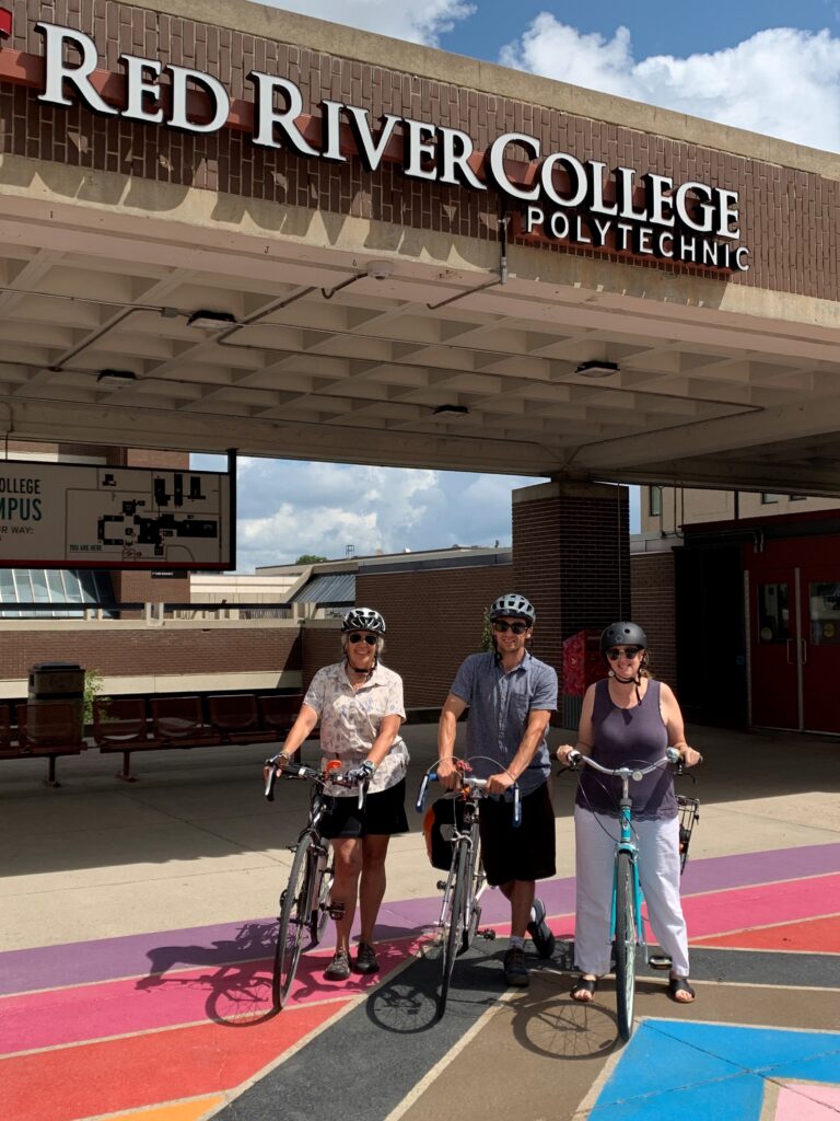Three staff members with bicycles standing in front of Red River College Polytechnic sign.