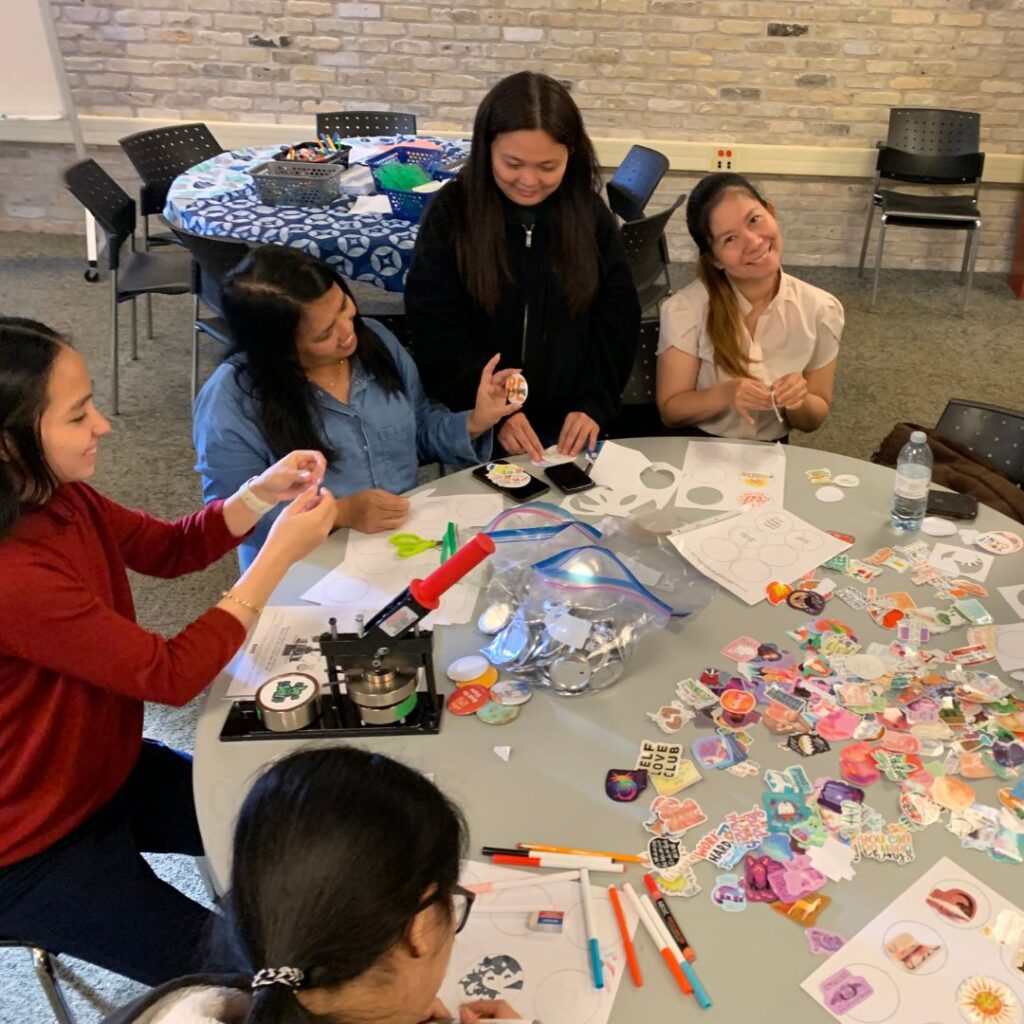 Group of students around a table making buttons, bracelets and other crafts.