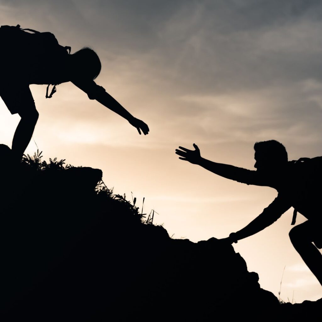 One hiker reaching out a hand to another hiker to help them uphill.