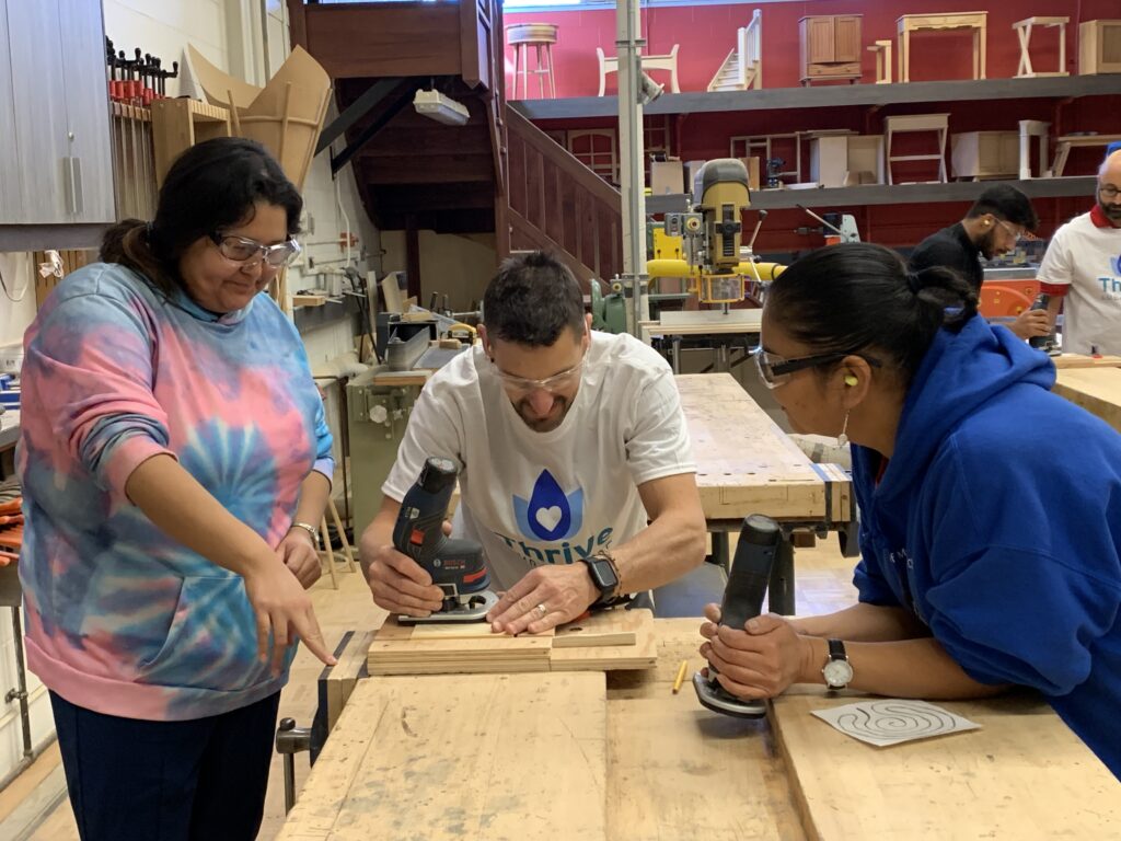 Two students in the woodshop with an instructor learning how to use a router and design a fidget.