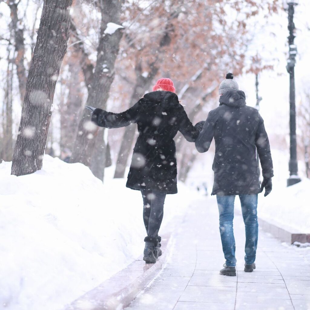 A couple walking hand in hand with light snow falling.