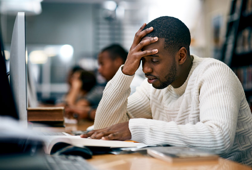 male student in white shirt reading text book with hand on forehead.