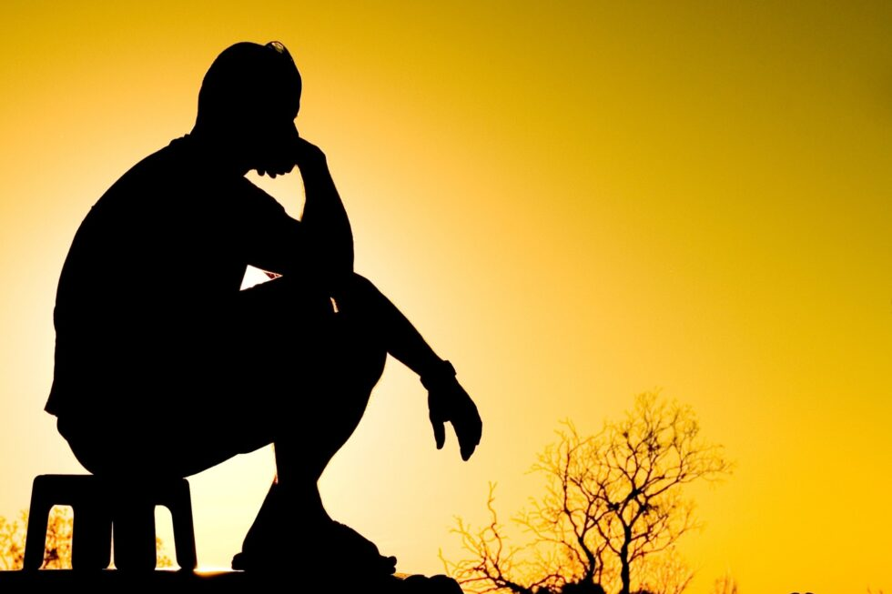silhouette of person sitting on a stool at sunset
