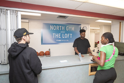 Photo of front desk at the north gym. Staff member helping two students.