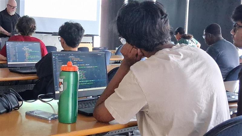 A group of students sitting in rows looking at their laptops, working on coding projects