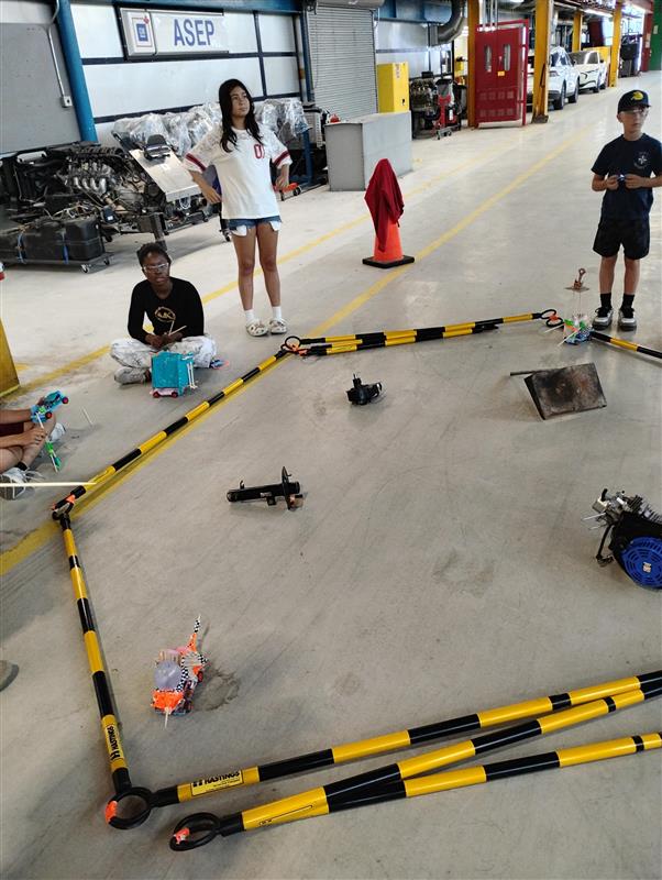 A group of campers are around a arena style set-up battling their RC cars