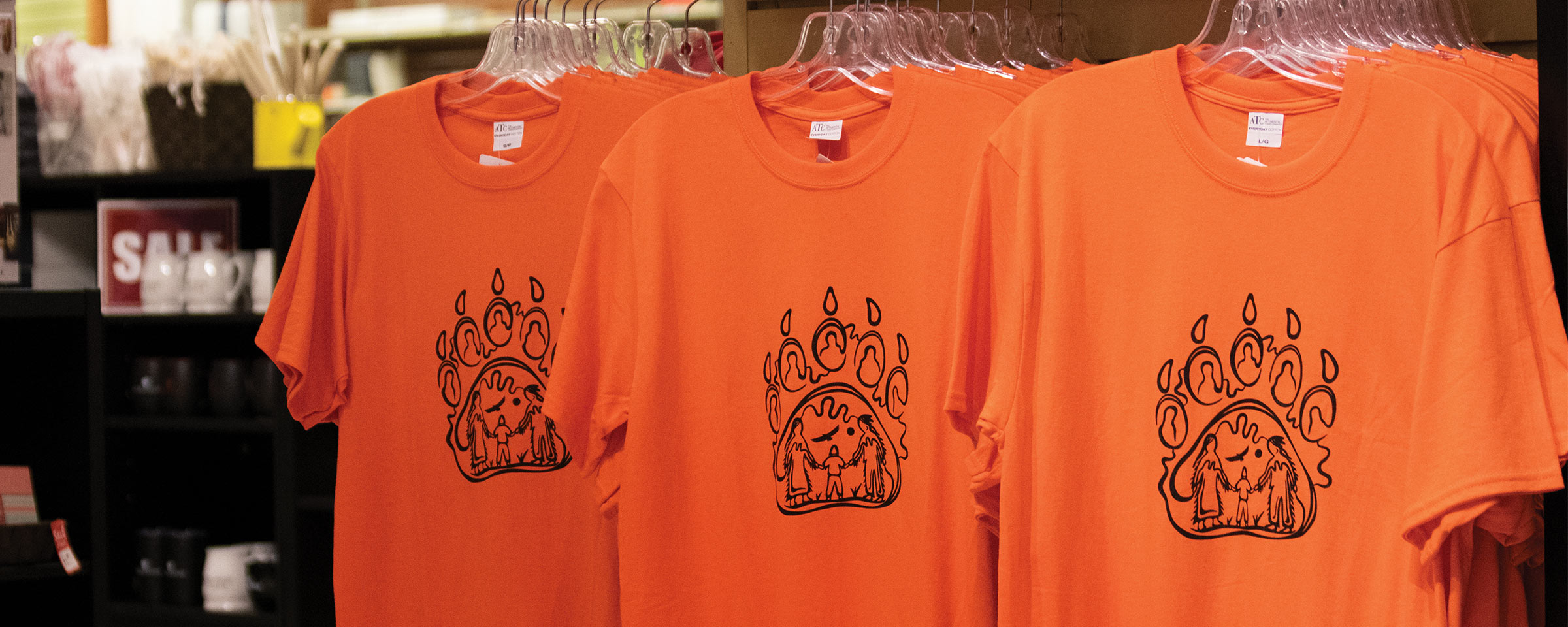 Three orange t-shirts on hangers in RRC Polytech's Campus Store