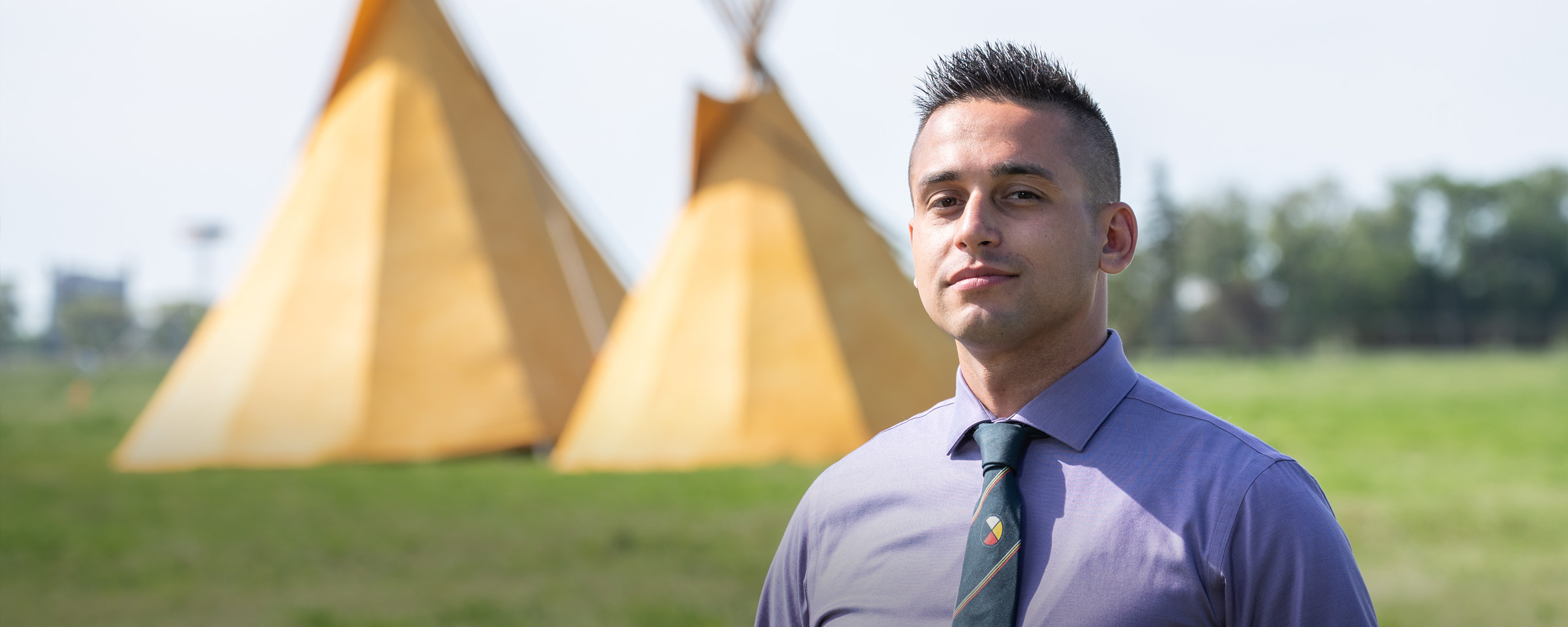 RRC Polytech grad Vic Savino, standing in front of two teepees.