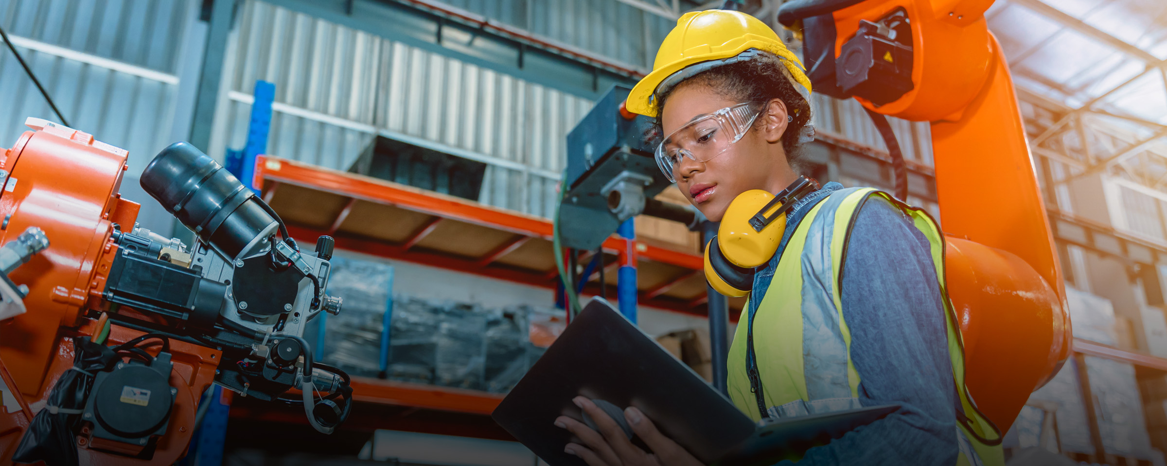 Woman with helmet clipboard programming a robotic welding machine.