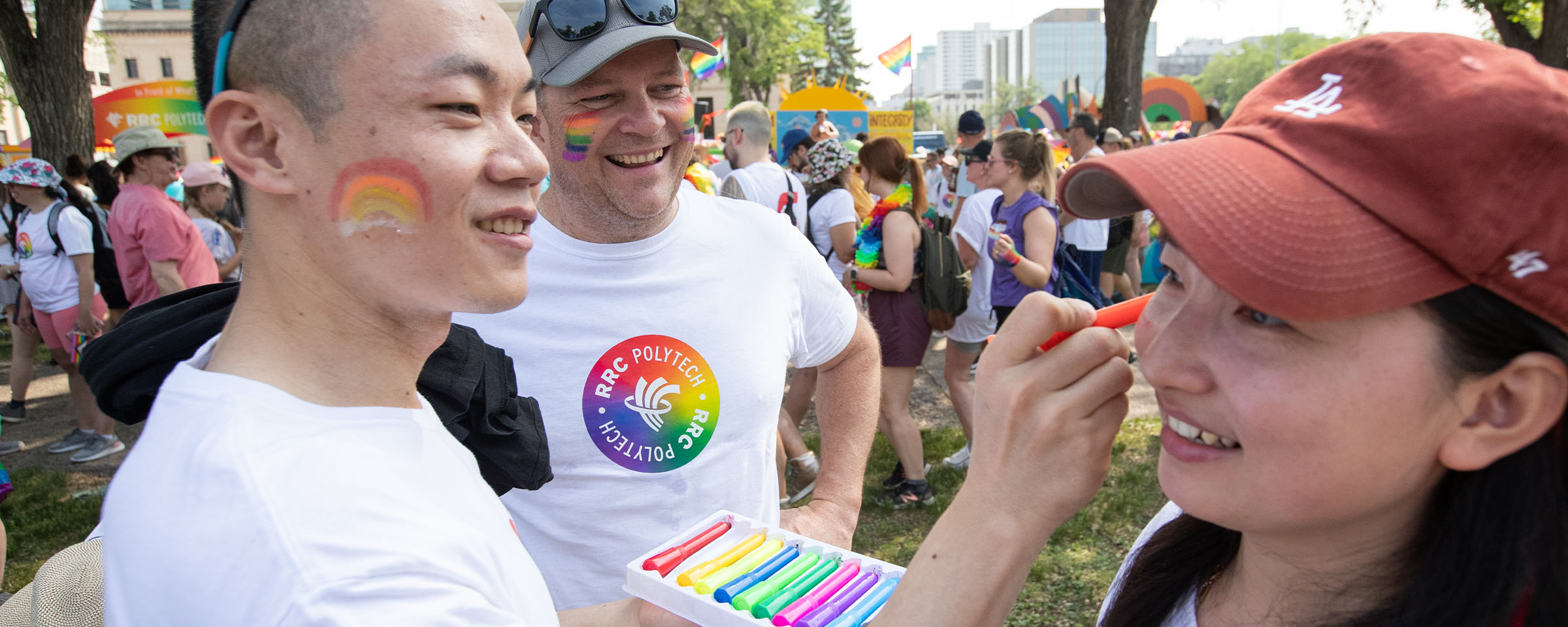 Male student painting female student's face at Pride Winnipeg Rally 2023.