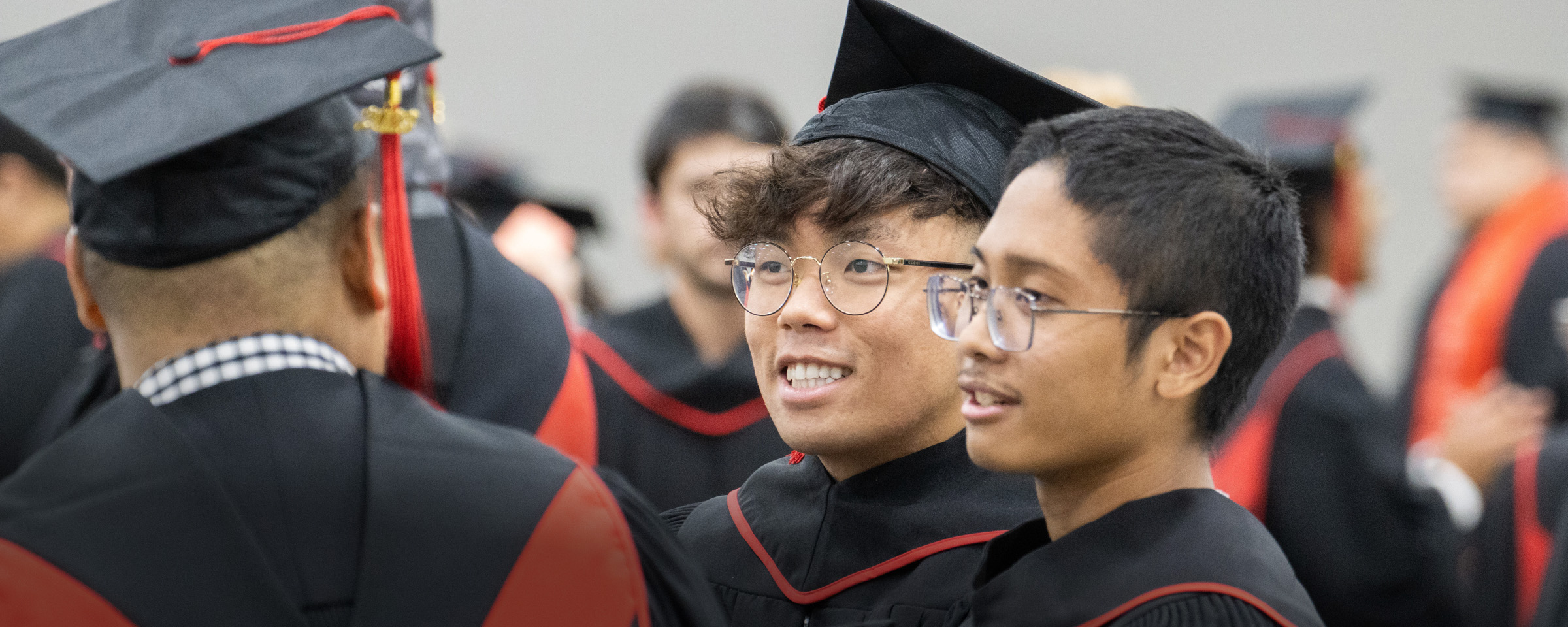 Two men with glasses, wearing black grad robes and mortarboards, talk to a friend at RRC Polytech's convocation ceremony.