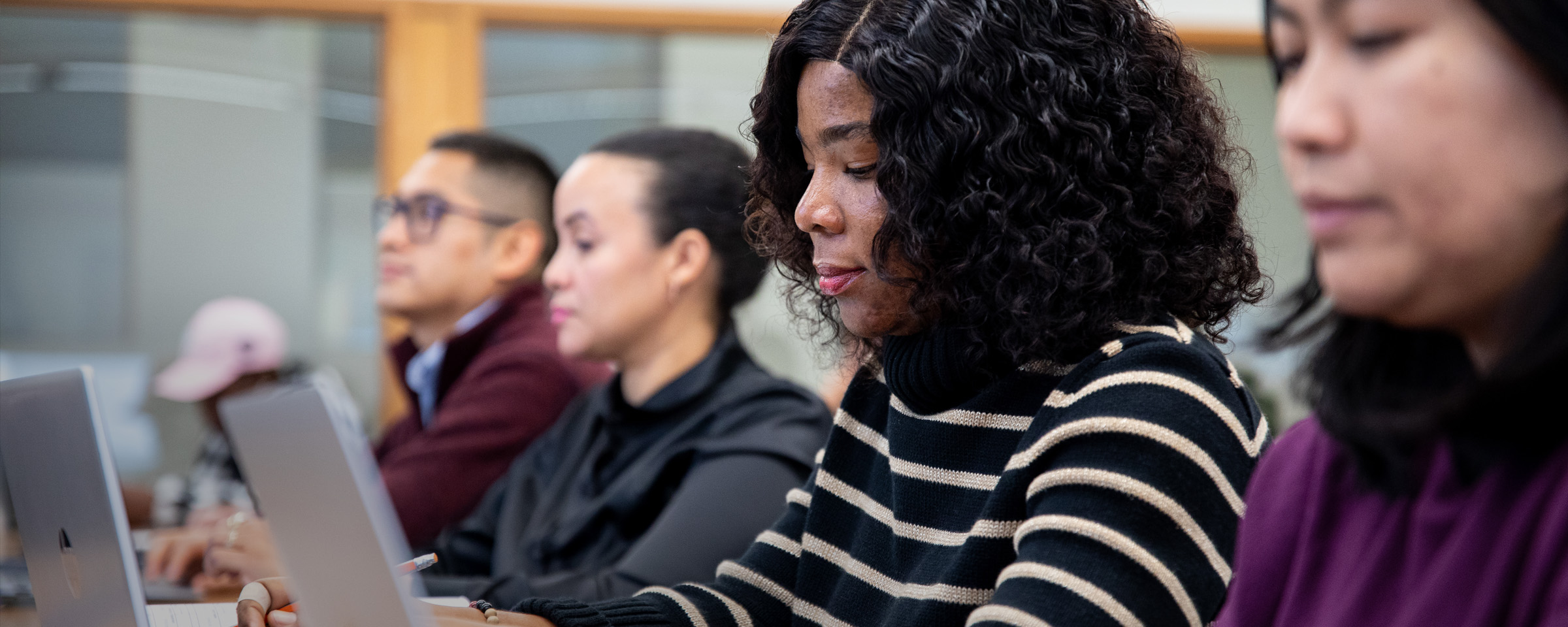 Row of four students — one man, three women — working on laptops. 
