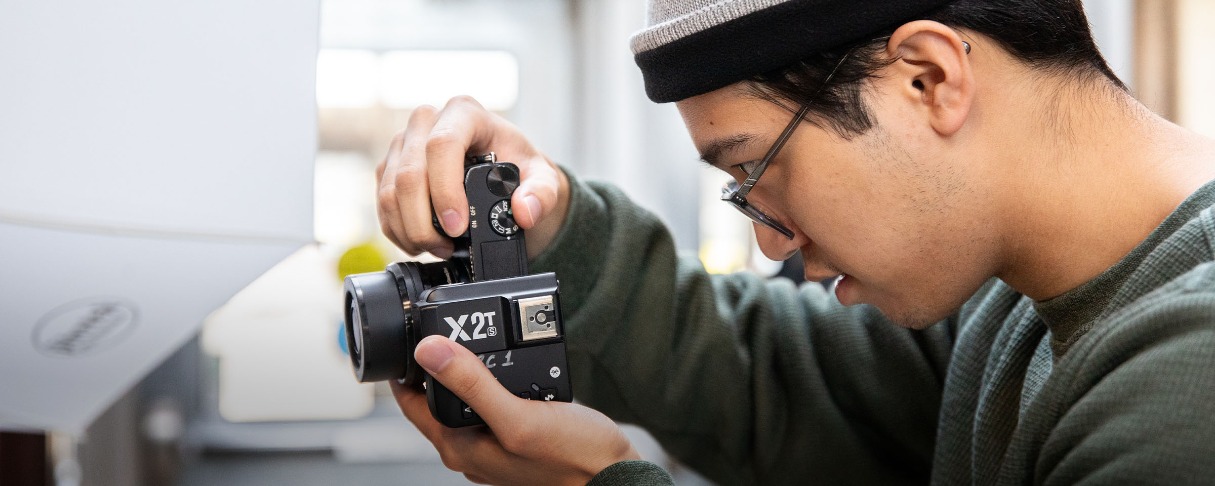 Close-up of male student wearing toque and glasses, peering into the viewfinder of a camera.