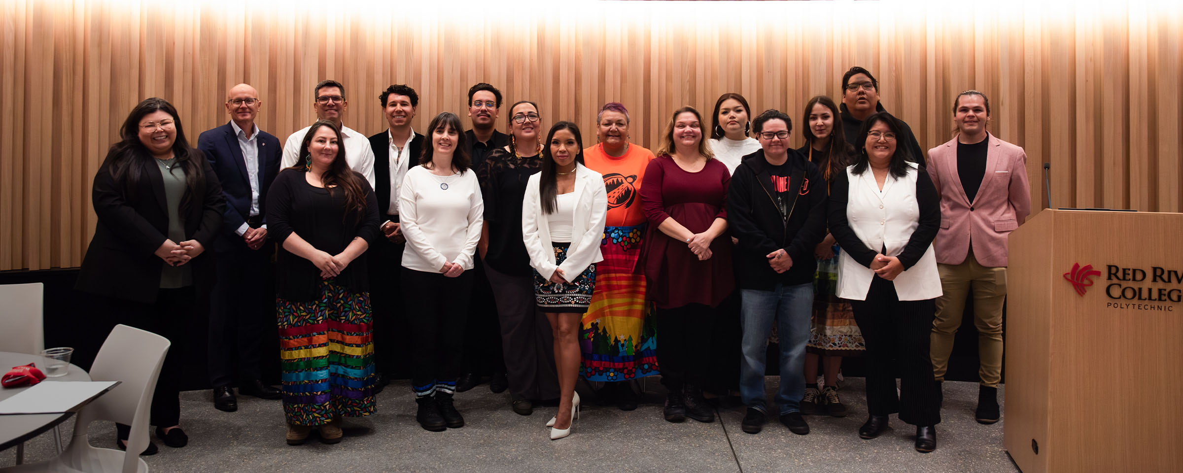 Group of Indigenous entrepreneurs and mentors standing in a row in RRC Polytech's Roundhouse Auditorium.
