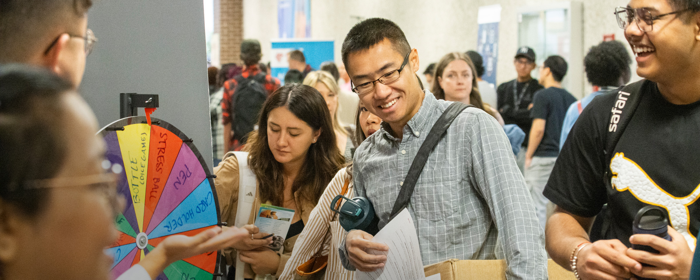 Smiling male students visit information booth during indoor student orientation event.