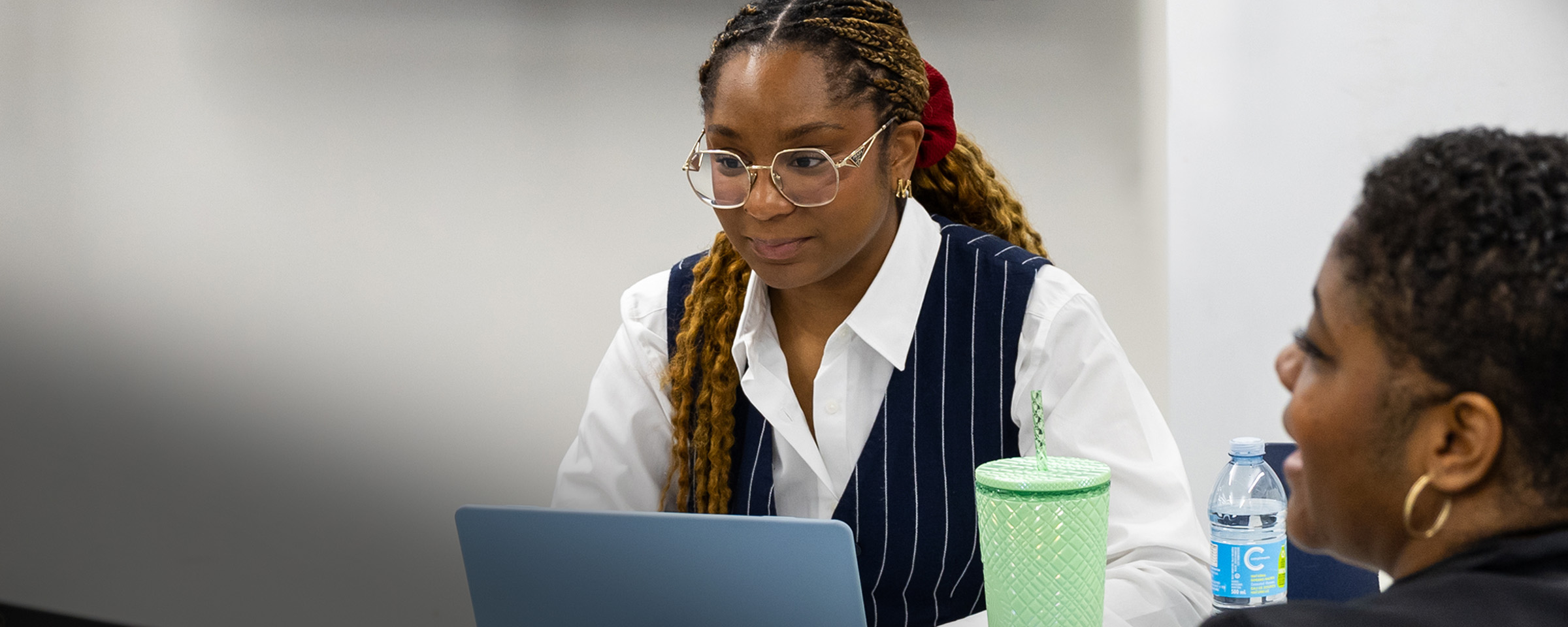 Young Black woman with striped vest and glasses working on a computer.