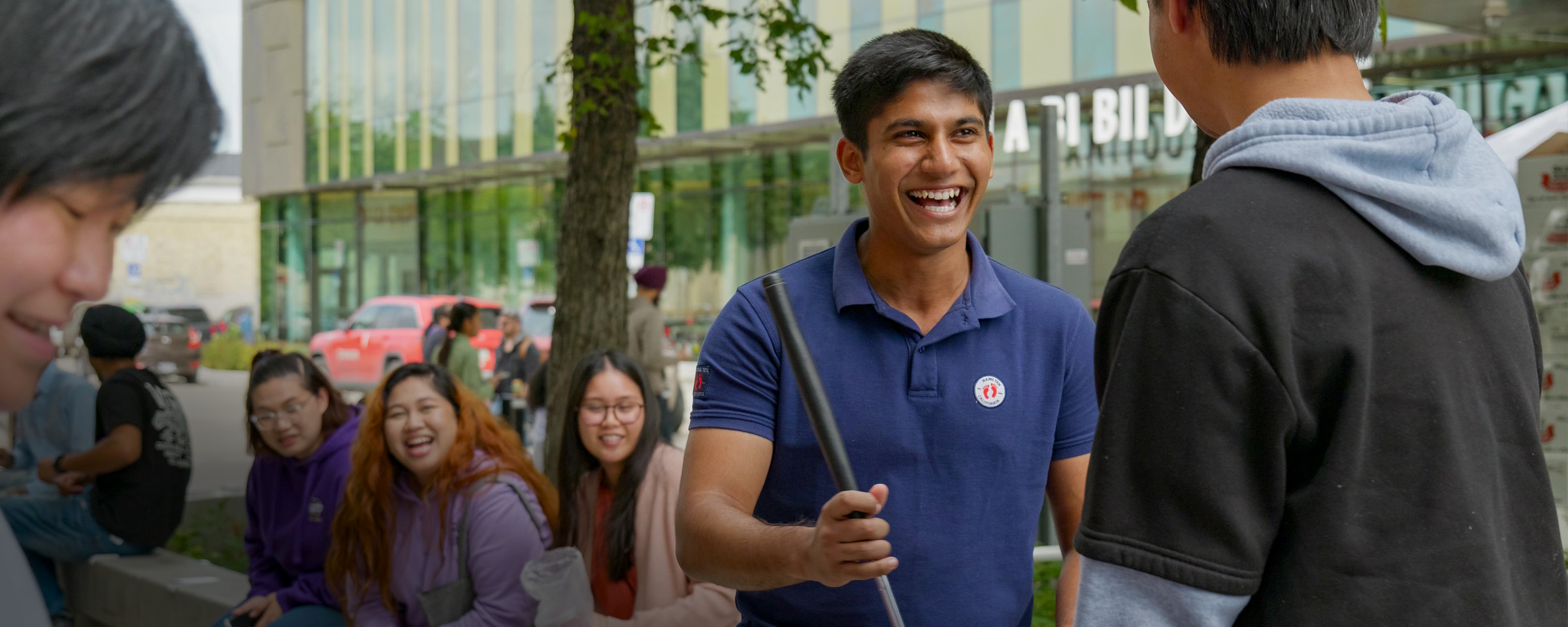Smiling male student playing shuffleboard in Roblin Centre courtyard as other smiling students look on.
