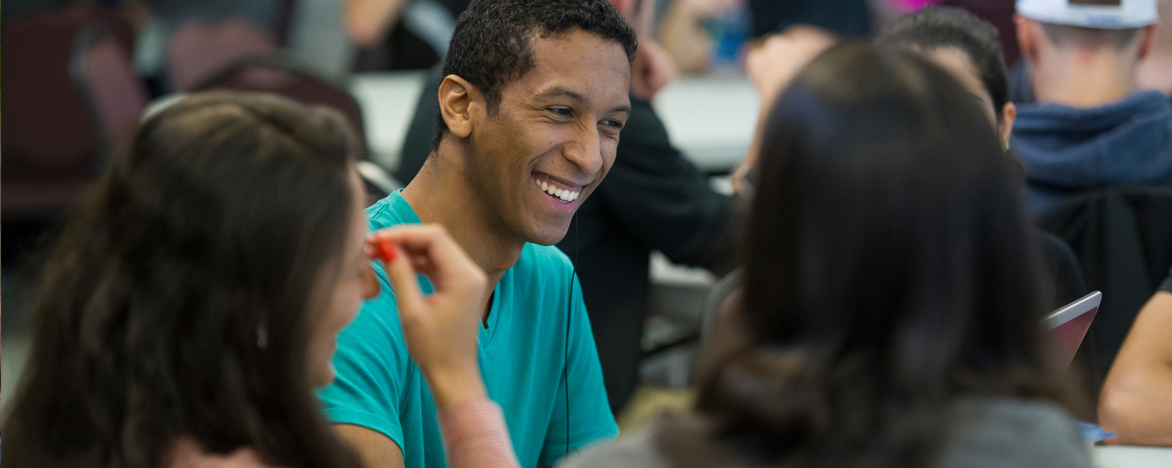 Laughing male student in conversation with others around a table.