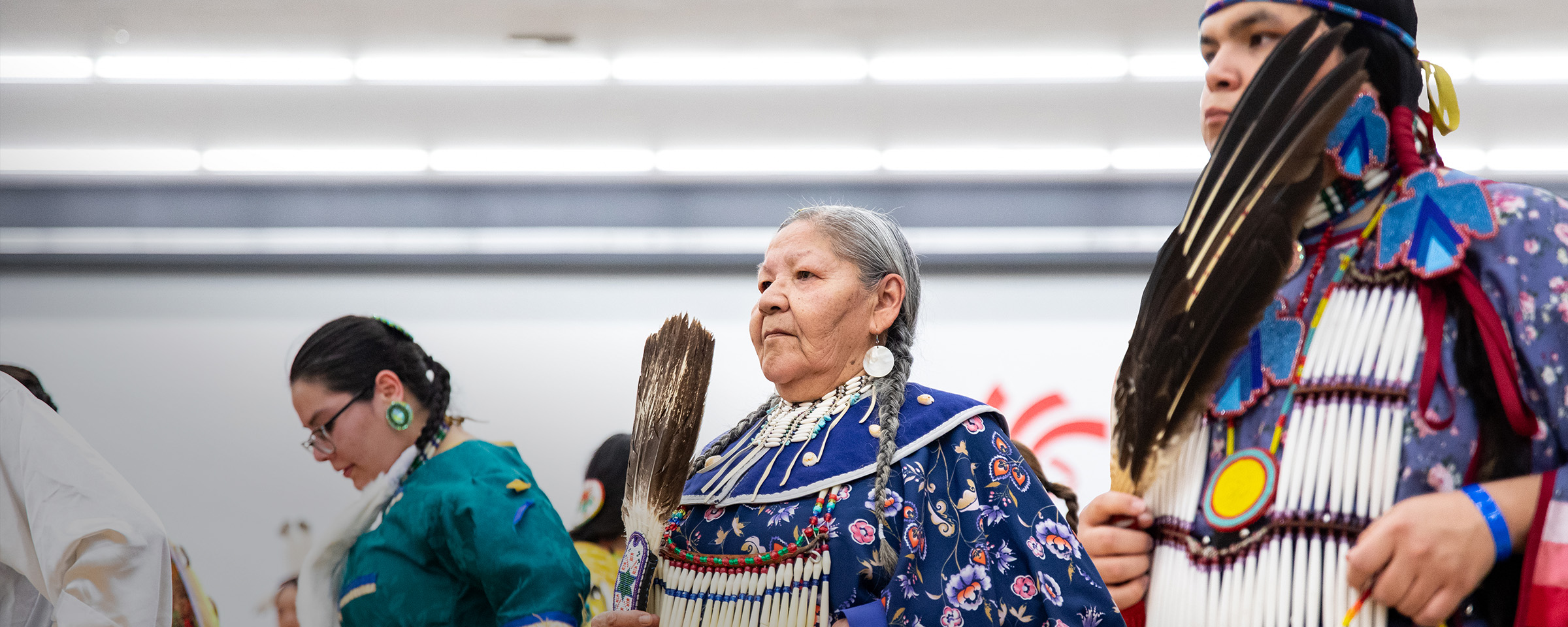 Profile view of three women wearing Indigenous regalia