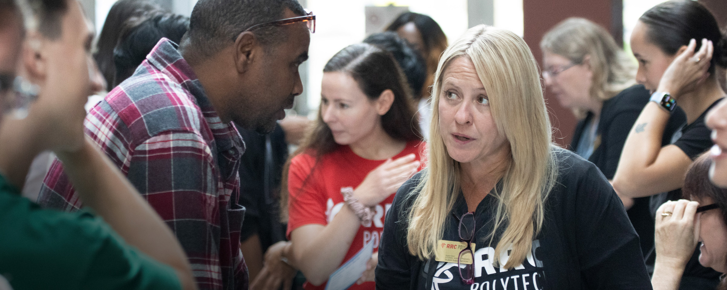 Woman in RRC Polytech t-shirt speaking to adult male student at orientation event.