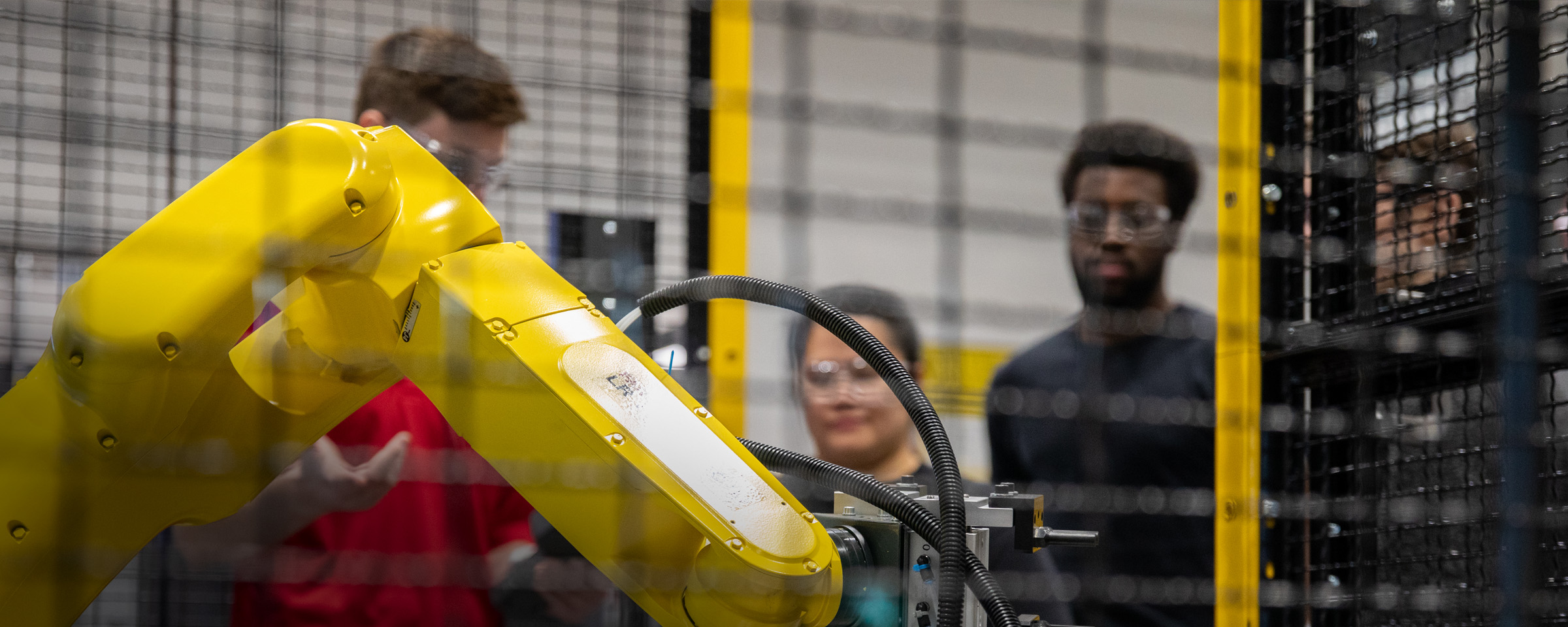 Students observe in background as instructor operates robotic arm.
